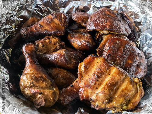 Close-up of freshly smoked chicken drumsticks and thighs served in aluminum foil after barbecue cooking