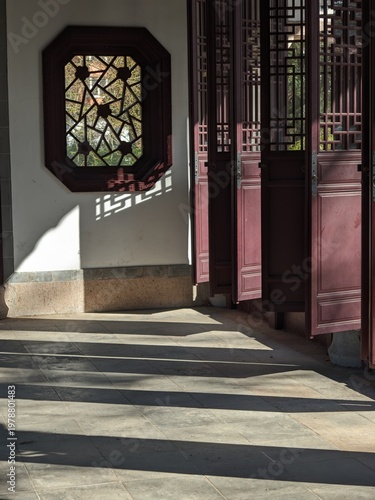 Intricate wooden window and open doors casting geometric shadows on a stone floor in China
