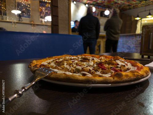 Mouth-watering chicken and pepper pizza with creamy white sauce served at a cozy restaurant.