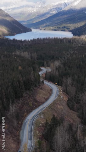 Aerial View of Winding Mountain Road Through Evergreen Forest Leading to a Serene Lake in British Columbia