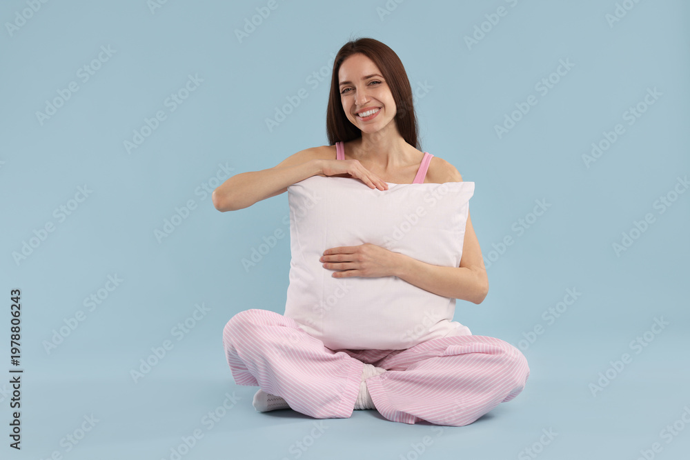 Obraz premium Beautiful woman with pillow on light blue background. Space for text