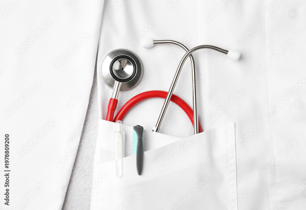 Fototapeta premium Stethoscope and pens in pocket of white doctor’s coat on light background, top view