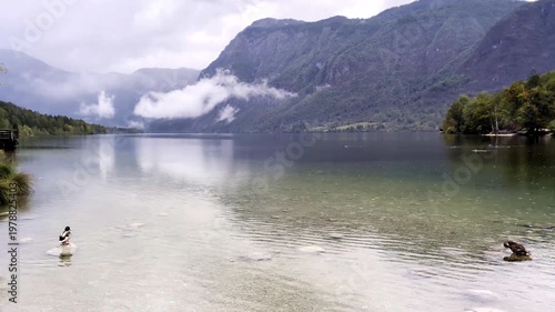 lake bohinj with mountains background (aerial view of famous alpine travel destination in slovenia) boat kayaking scenic european tourism getaway (julian alps, europe) rain view scenic landscape