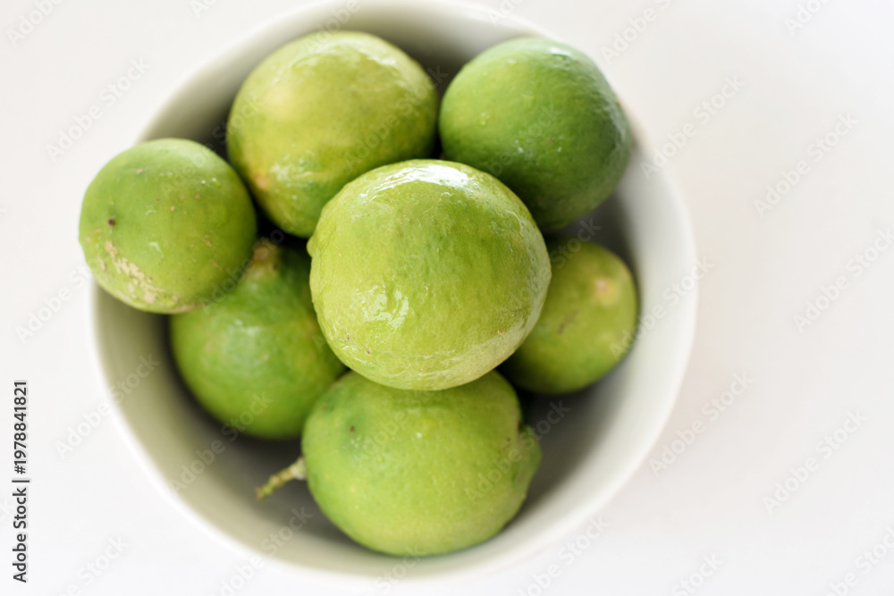 Obraz premium Top view of fresh green limes arranged on a clean white table, creating a bright and minimal citrus background. Ideal for concepts of freshness, healthy lifestyle, natural ingredients, summer drinks,