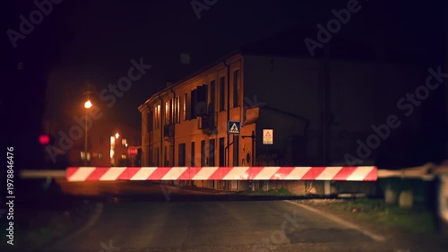 Night video of a closed railway crossing in a village street with houses nearby. Warning lights active while a train covered with graffiti passes through. Atmospheric scene combining transport