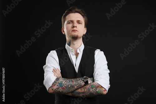 Foto Young man with tattoos in stylish vest and shirt on black background
