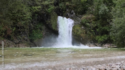 beautiful scenic small waterfall in forest next to farm river and bike trail in bohinj slovenia europe (stunning landscape julian alps alpine mountains scenery) trees woods hiking hike path trail