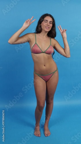 Playful woman in bikini dancing and making peace signs