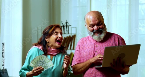 Senior Indian couple holding a five hundred rupee money fan with a laptop, looking surprised and joyful while cash is raining from above to denote sudden growth