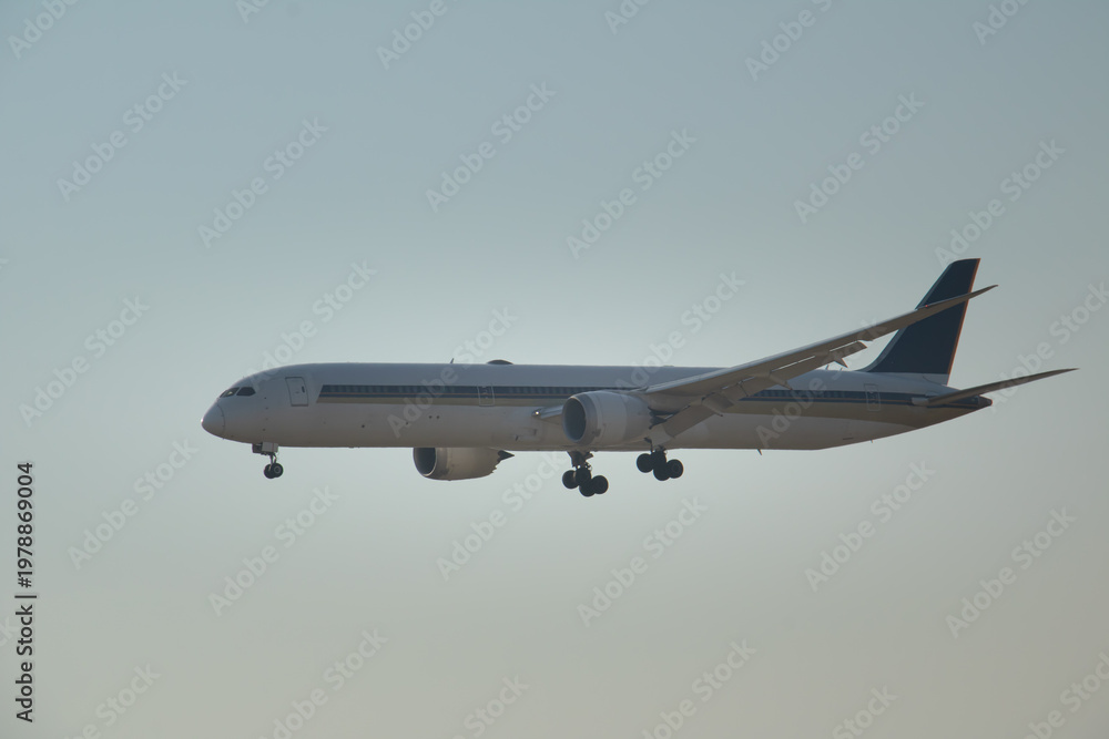 Fototapeta premium Large commercial airplane flying low during final approach phase, isolated against soft sky background with ample copy space for aviation, travel, and logistics concepts.
