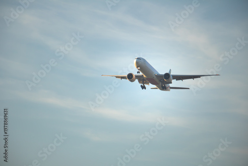 Tableau sur toile Front view of a twin-engine passenger airplane on final descent with landing gear down, flying through a soft clouded sky, suitable for aviation, travel, and global transportation themes