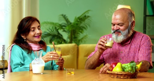 Senior Indian couple sitting at a breakfast table in their modern home, drinking healthy turmeric milk, also known as haldi or golden milk, for wellness