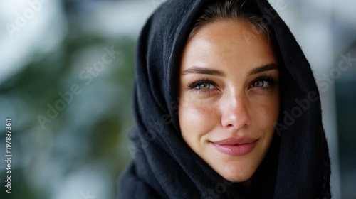 Woman Smiling While Wearing a Dark Hooded Garment in a City Setting During Da...