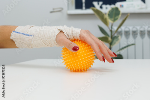 Injured hand rolling an orange rehabilitation ball with spikes on a table