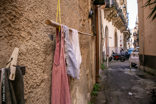 Narrow residential street in Palermo featuring rustic yellow-toned buildings, laundry hanging between balconies, and potted plants along the alleyway, capturing authentic local lifestyle
