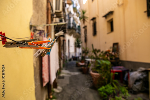 Narrow residential street in Palermo featuring rustic yellow-toned buildings, laundry hanging between balconies, and potted plants along the alleyway, capturing authentic local lifestyle