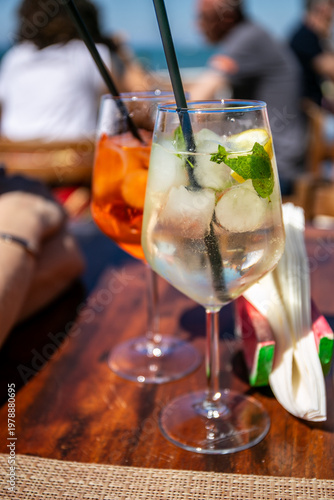 Vibrant Italian spritz cocktails served in large wine glasses over ice, featuring a clear Hugo Spritz with prosecco, elderflower liqueur, mint, and lemon in the foreground, and an orange Aperol-style 
