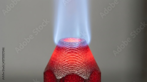 A close-up view of a red glass object emitting a vibrant blue flame against a gray background