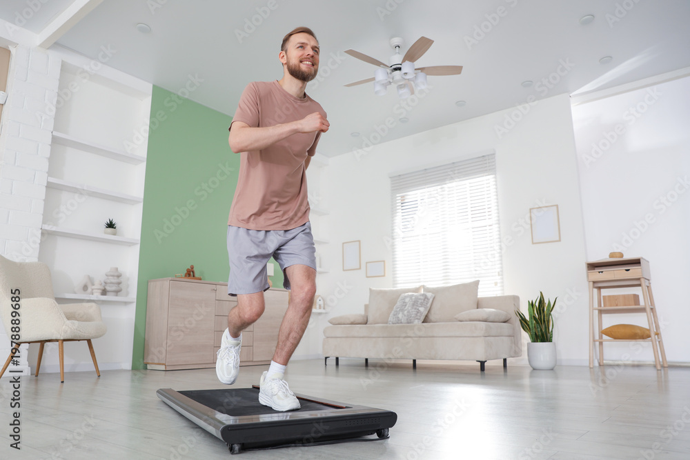 Fototapeta premium Sporty man training on treadmill at home, low angle view. Space for text
