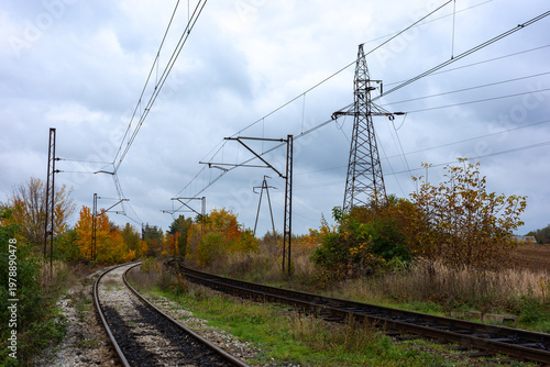 Electric traction above the tracks of an old railway line. High-voltage pylons in the background. Photo taken on a cloudy autumn day.