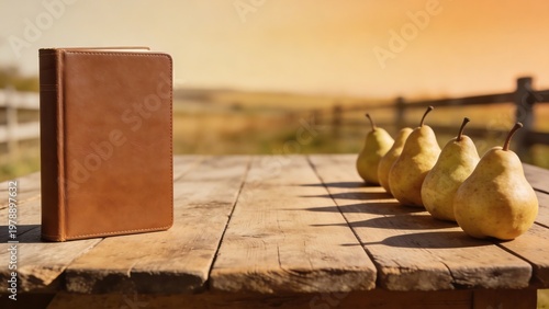 A leather-bound book stands beside a row of ripe pears on a rustic wooden table