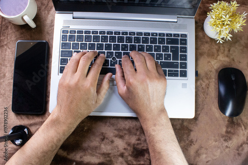 Man typing on laptop keyboard at home office workspace with smartphone coffee and accessories top view