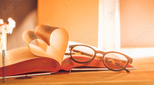 Obraz na plátně Open book with pages shaped like a heart beside glasses and a flower on a wooden