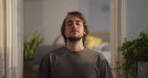 A young man finds peace meditating in a sunny, plant-filled room, enjoying quiet moments of stillness
