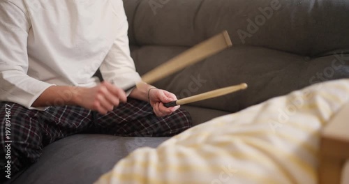 A person joyfully plays wooden sticks on the couch, filling the home with infectious energy and lively beats