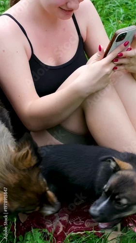 Teen girl sitting on red mat with mother dog and puppy playing nearby trusting yet careful playful interaction outdoors