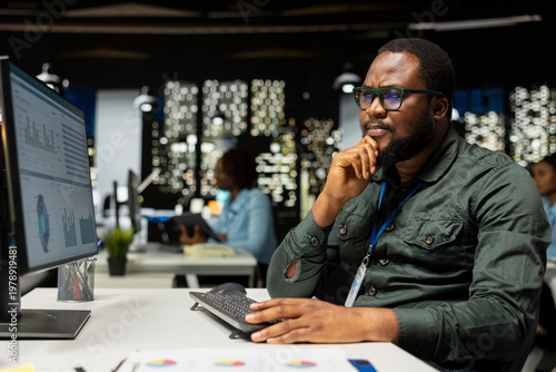 Office worker reviewing KPI metrics on monitor and analytics on desktop, building a vision and business strategy to accomplish objectives and success. Professional mindset after hours.