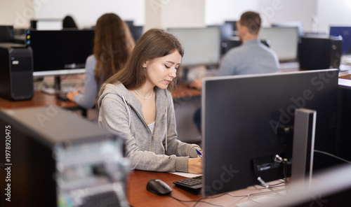 Obraz na płótnie Young woman taking notes while working on computer in office space