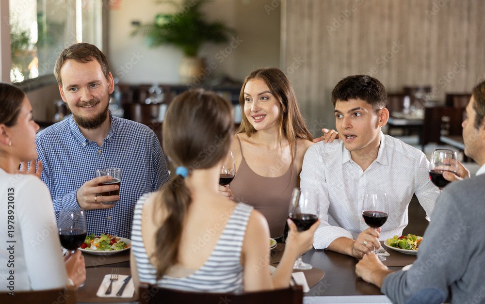 Obraz premium Group of men and women friends eating drinking and talking in restaurant