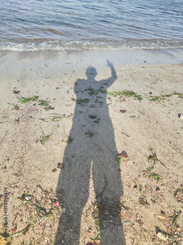 Human shadow waving hand on sandy beach