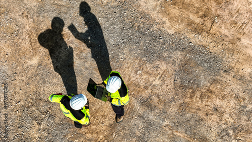 Obraz na płótnie Aerial top down view of two engineers in safety gear discussing a project on a digital tablet