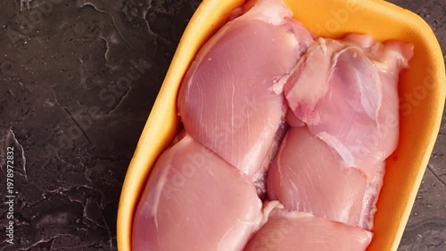 Delicious chicken thighs displayed in a vibrant yellow tray sitting on a textured dark surface, ideal for meal prep.