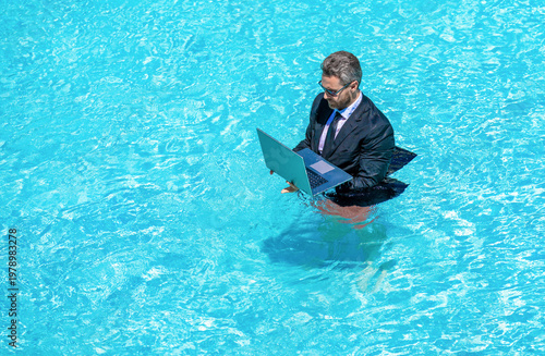 Businessman in suit with laptop in swimming pool. Crazy business man on summer vacation. Remote working. Summer business vacation. Funny crazy businessman rest in formal wear in pool, banner