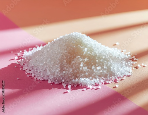 Pile of granulated sugar on a pink and beige background with soft shadows