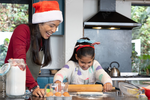 Asian mother and child baking together at home kitchen using rolling pin, wearing Santa hat