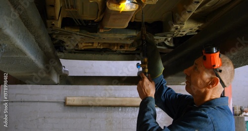 Torching mechanic in blue coverall with red earmuffs, working on undercarriage on lift, copy space