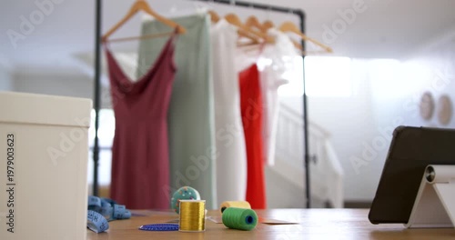 Camera tilting up, revealing four dresses and spools with tablet in sewing studio showing garments