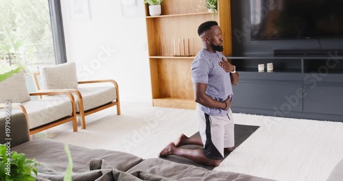 African American man kneeling on black mat at home, tee, hands on chest, stomach, copy space