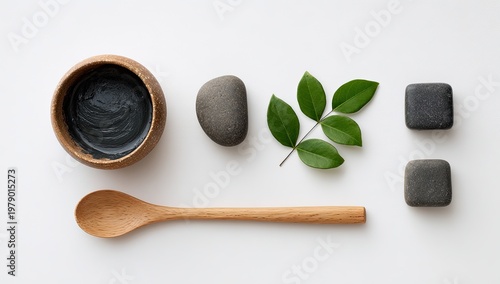 Spa-themed flat lay featuring wooden bowl with mud, stones, leaf, and spoon on white