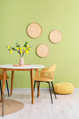 Vase with lemon tree branches on dining table near green wall in room