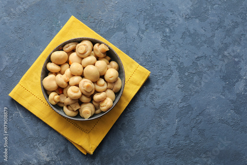 Bowl with tasty canned mushrooms on blue background