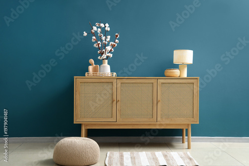Interior of stylish room with wooden cabinet, pouf and cotton flowers