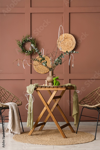 Dining table with tree branches and Easter wreath on brown wall in room