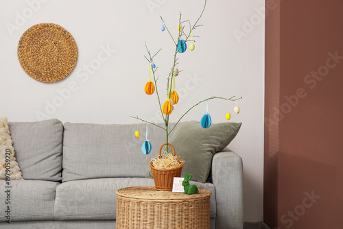 Interior of festive living room with grey sofa and tree branches decorated with Easter eggs on wicker coffee table