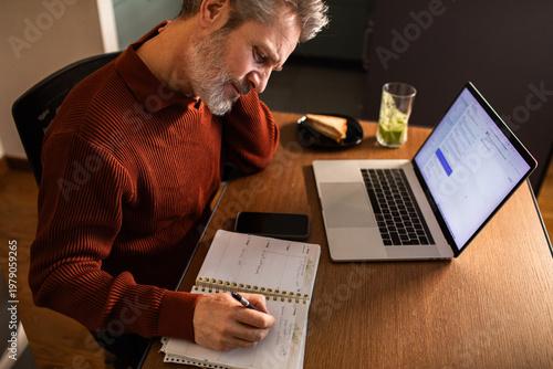 Mature man writing in planner at home office desk