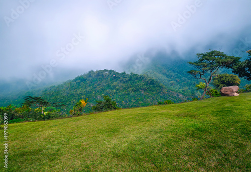 Green mountains contrast with the blue sky and a light mist.